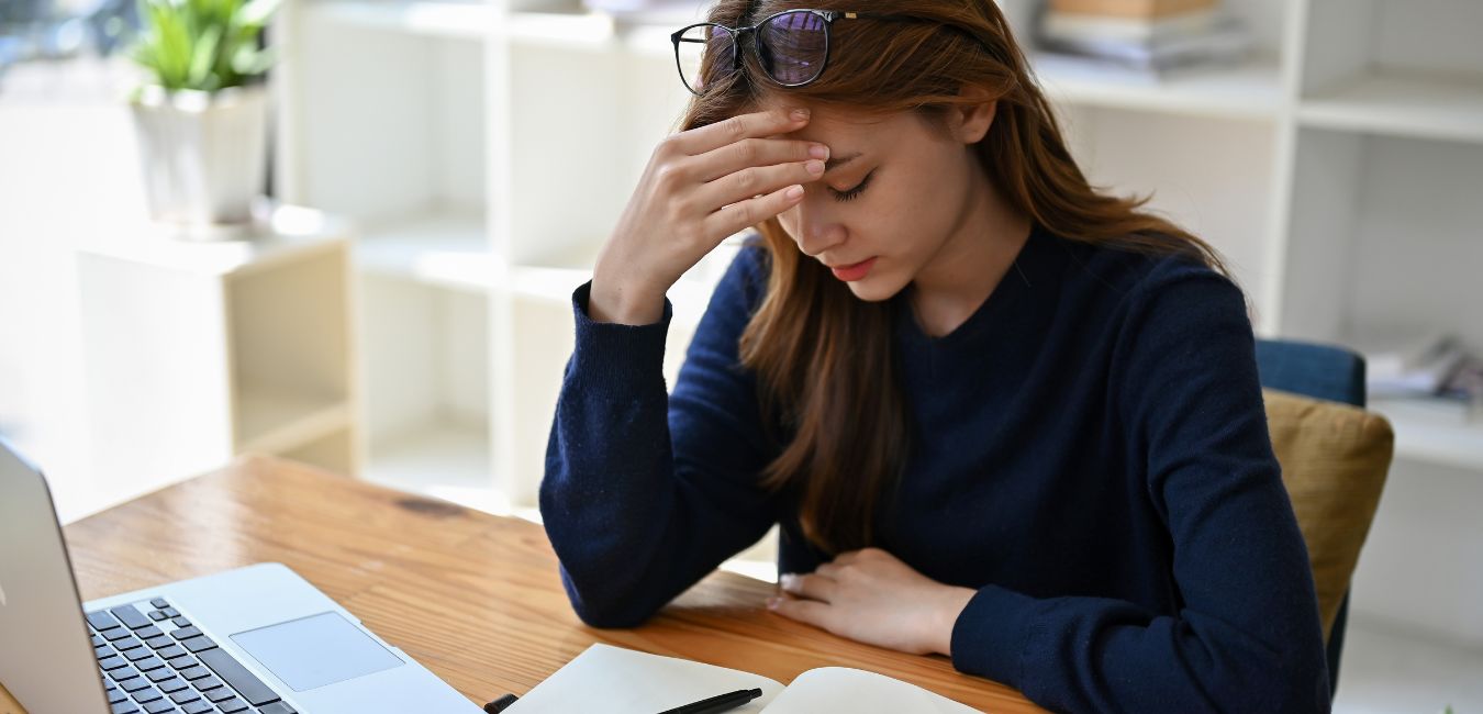 A person sat at a desk looking stressed with hand to forehead